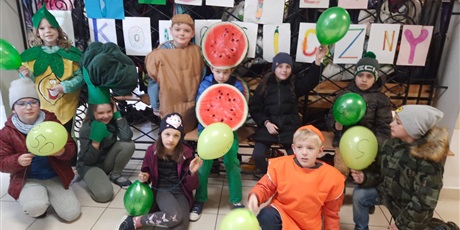 Powiększ grafikę: Uczniowie przebrani za owoce i warzywa stoją na tle napisu reklamującego Tydzień Ekologiczny