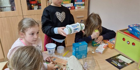 Powiększ grafikę: Cztery dziewczynki przy stoliku wykonują zabawki z materiałów do recyklingu.