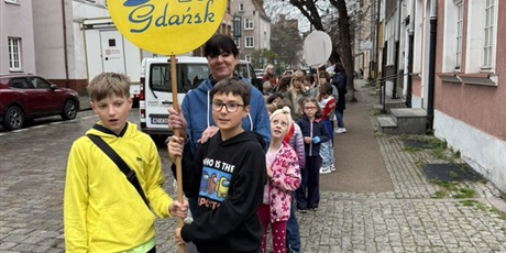 Powiększ grafikę: Uczniowie podczas przemarszu ulicami Gdańska. Trzymają w rękach logo szkoły.