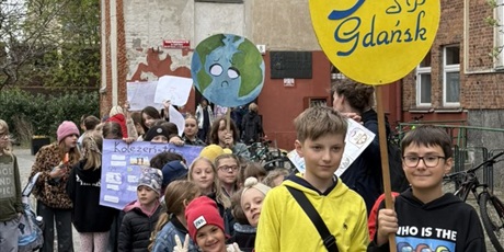 Powiększ grafikę: Uczniowie podczas przemarszu ulicami Gdańska. Trzymają w rękach logo szkoły i plakaty z ekologicznymi hasłami.