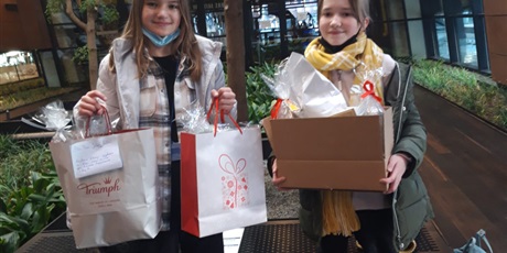 Powiększ grafikę: Dwie dziewczynki w torbach i kartonie trzymają dary "Dobroci na święta" dla Hospicjum.