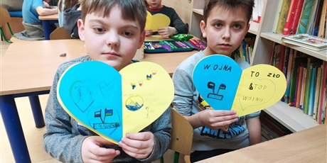 Powiększ grafikę: Dwóch chłopców pokazuje żółto-niebieskie serca z napisami przeciw wojnie.