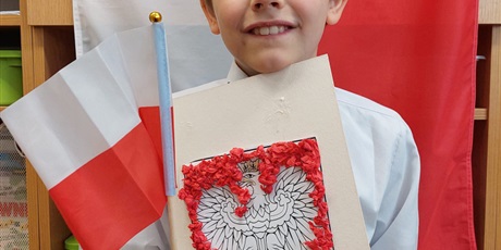Powiększ grafikę: Uczeń kl. IIIa na tle flagi państwowej prezentuje wykonaną pracę  plastyczną podczas klasowych obchodów Święta Niepodległości