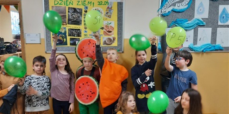 Powiększ grafikę: Dzieci w przebraniu za owoce i warzywa z balonami na tle ekspozycji z okazji Dnia Ziemi