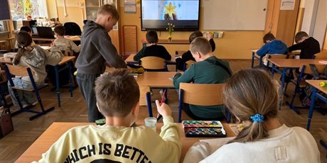Powiększ grafikę: Uczniowie w sali lekcyjnej wykonują prace plastyczne. Na stoliku ustawione są żonkile.