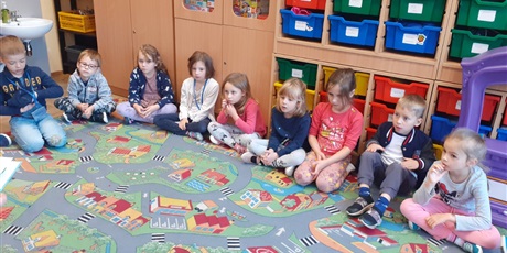 Powiększ grafikę: Dzieci z kl. 0a słuchają czytanej książki przez p. Mirkę z biblioteki. Dzieci siedzą na dywanie.
