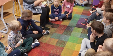 Powiększ grafikę: Dzieci z kl. IIb słuchają czytanej książki przez p. Mirkę z biblioteki. Dzieci siedzą na dywanie.