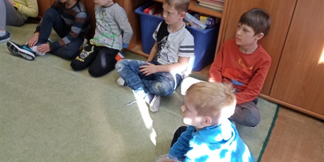 Powiększ grafikę: Dzieci z kl. Ib słuchają czytanej książki przez p. Mirkę z biblioteki. Dzieci siedzą na dywanie.