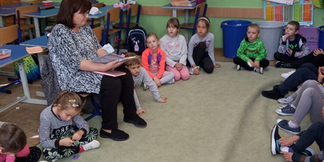 Powiększ grafikę: Dzieci z kl. Ib słuchają czytanej książki przez p. Mirkę z biblioteki. Dzieci siedzą na dywanie.