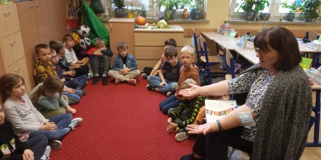 Powiększ grafikę: Dzieci z kl. IIa słuchają czytanej książki przez p. Mirkę z biblioteki. Dzieci siedzą na dywanie.