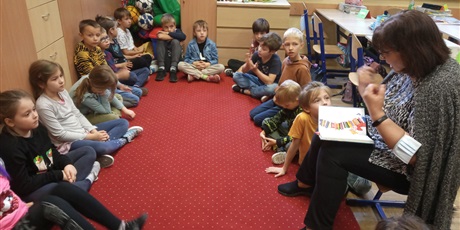 Powiększ grafikę: Dzieci z kl. IIa słuchają czytanej książki przez p. Mirkę z biblioteki. Dzieci siedzą na dywanie.