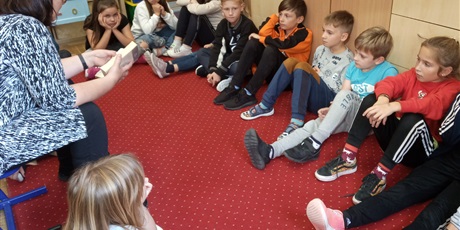 Powiększ grafikę: Dzieci z kl. IIIb słuchają czytanej książki przez p. Mirkę z biblioteki. Dzieci siedzą na dywanie.