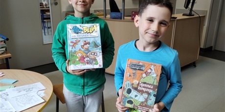 Powiększ grafikę: Dwóch chłopców w bibliotece, trzymają w dłoniach książki.
