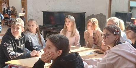 Powiększ grafikę: Uczniowie i nauczyciele siedzą przy stolikach i z uwagą słuchają wykładu.